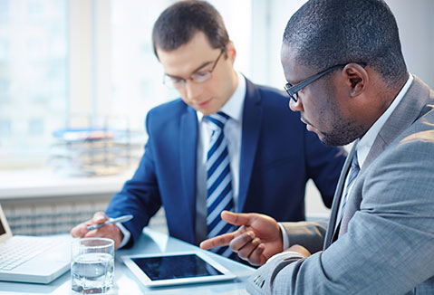 Two men discussing something that is displayed on a tablet.
